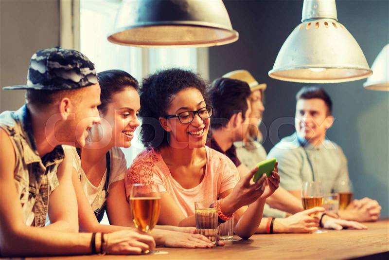 People, leisure, friendship, technology and communication concept - group of happy smiling friends with smartphone and drinks at bar or pub, stock photo