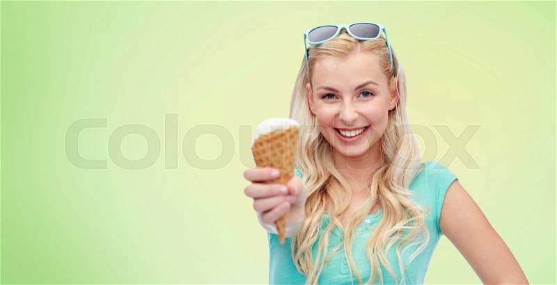 Summer, junk food and people concept - young woman or teenage girl in sunglasses eating ice cream over green natural background, stock photo