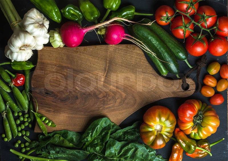 Fresh raw vegetable ingredients for healthy cooking or salad making with dark wooden cutting baoard in center, top view, copy space. Diet or vegetarian food concept, horizontal composition, stock photo