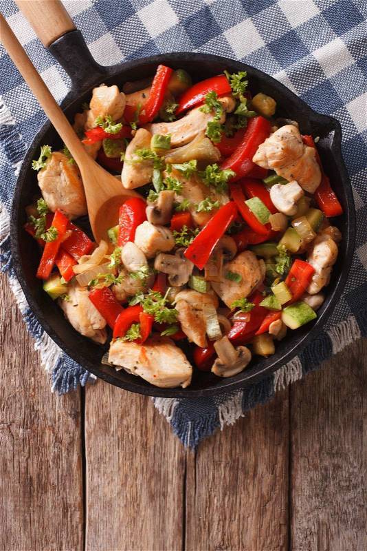 Stir Fry Chicken with mushrooms, peppers and zucchini on a frying pan close-up. Vertical view from above\, stock photo