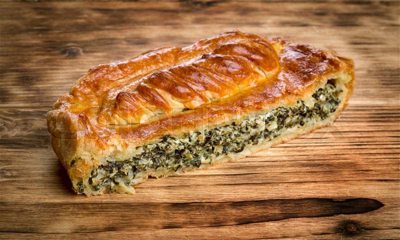 Close up view of fresh backed spinach pie on wooden background, stock photo
