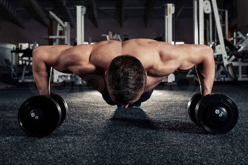 Handsome muscular man doing pushup exercise with dumbbell in a crossfit workout, stock photo