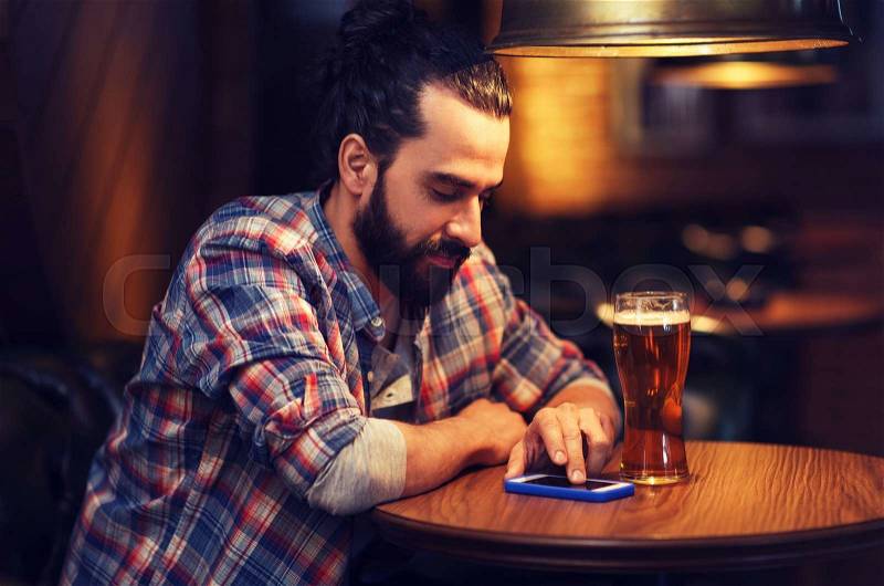 People and technology concept - happy man with smartphone drinking beer and reading message at bar or pub, stock photo
