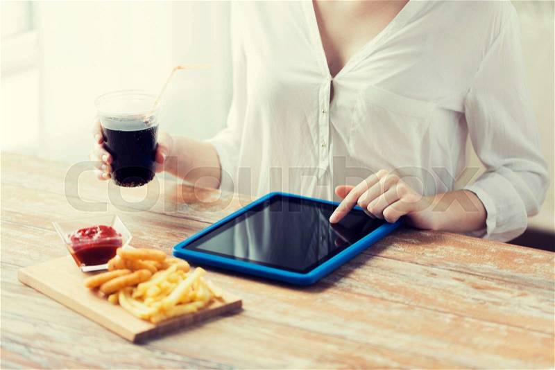 Fast food, people, technology and diet concept - close up of woman with tablet pc computer eating french fries with ketchup, deep-fried squid rings and cola at wooden table, stock photo