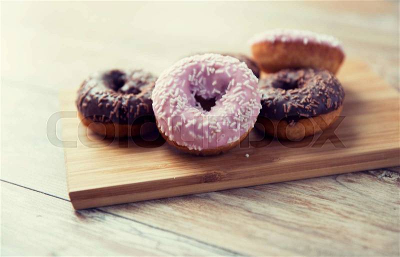Fast food, junk-food, baking, sweets and unhealthy eating concept - close up of glazed donuts on wooden board on table, stock photo