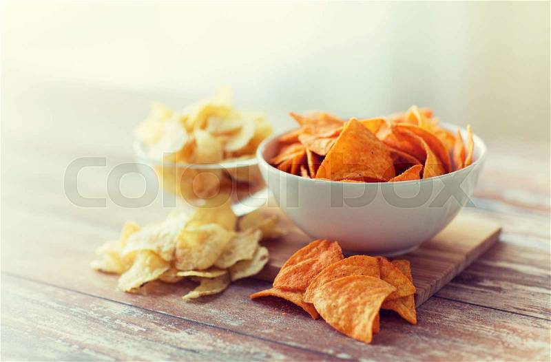 Fast food, junk-food, cuisine and unhealthy eating concept - close up of crunchy potato crisps and corn crisps or nachos in bowls, stock photo