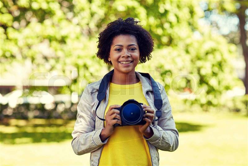 People, photography, technology, leisure and lifestyle - happy young african american female photographer with digital camera in summer park, stock photo
