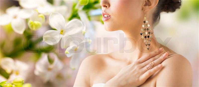 Glamour, beauty, jewelry and luxury concept - close up of beautiful woman with earrings over natural spring lilac blossom background, stock photo