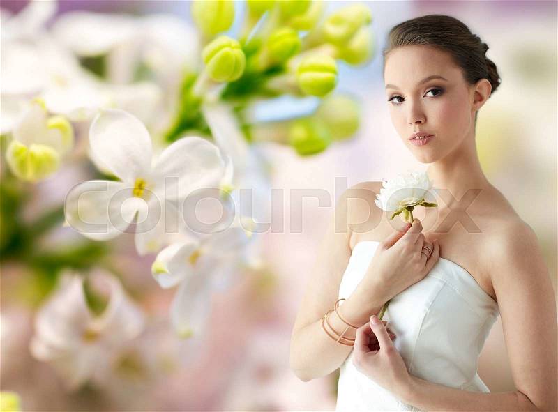 Beauty, jewelry, people and luxury concept - beautiful asian woman or bride in white dress with peony flower, golden ring and bracelet over natural spring lilac blossom background, stock photo