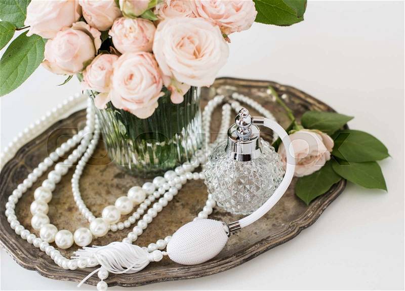 Elegant composition in retro style, vintage perfume bottle and a bouquet of roses on a silver tray on ladies dressing table, stock photo