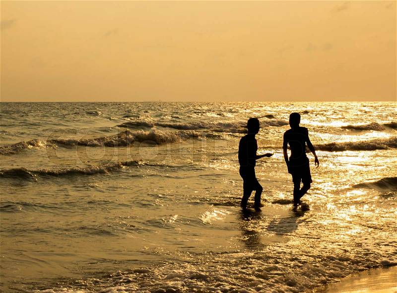 Silhouette of two people walking on beach at sunset, stock photo