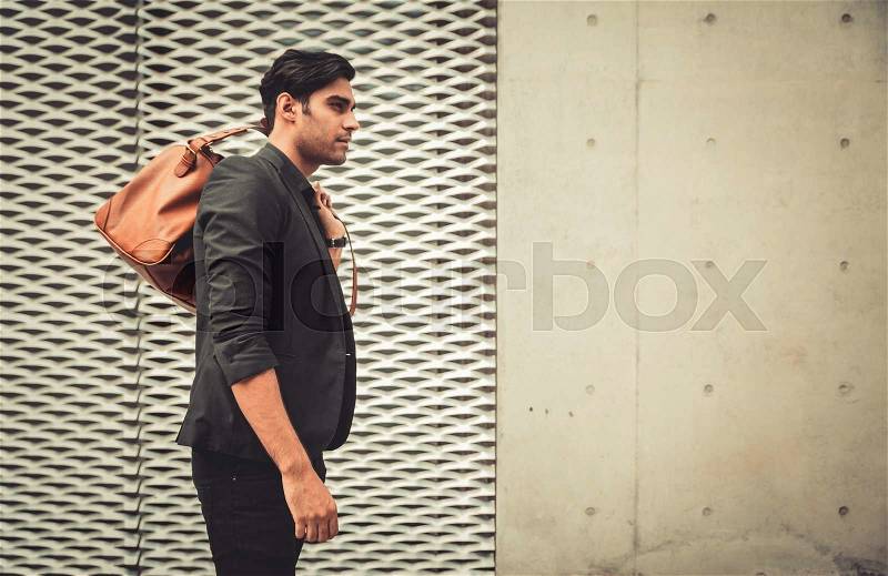 Stylish model looking man profile with handbag on his shoulder in modern architectural environment, stock photo