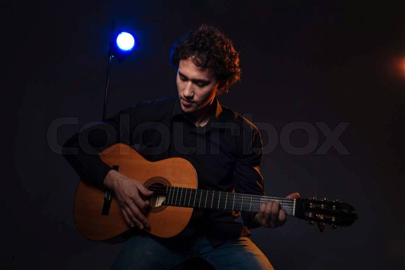 Young man playing on guitar over dark background, stock photo