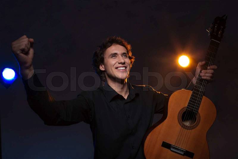 Happy man with a guitar gets applause over dark background, stock photo