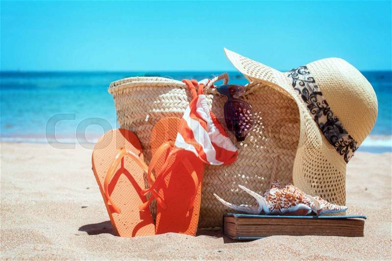 Sunbathing accessories on sandy beach in straw bag, summer relaxation concept, retro toned, stock photo