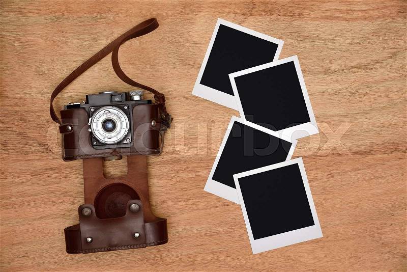 Old vintage camera in a leather case with four blank photo on wooden desk, stock photo