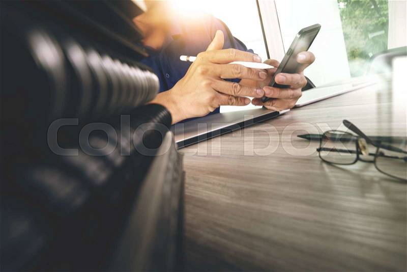 Designer hand working with digital tablet and laptop computer and book stack and eye glass on wooden desk as concept, stock photo
