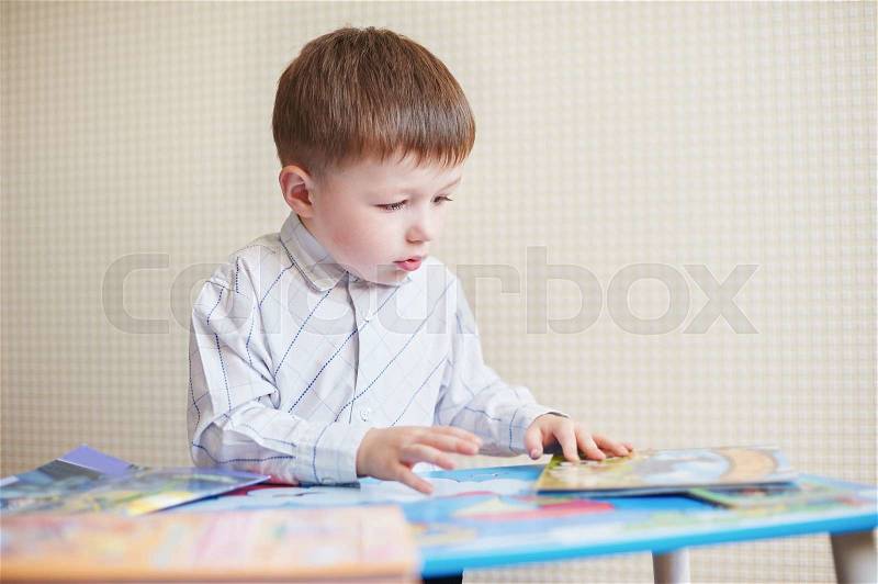 Little boy is sitting at the desk and read book, stock photo
