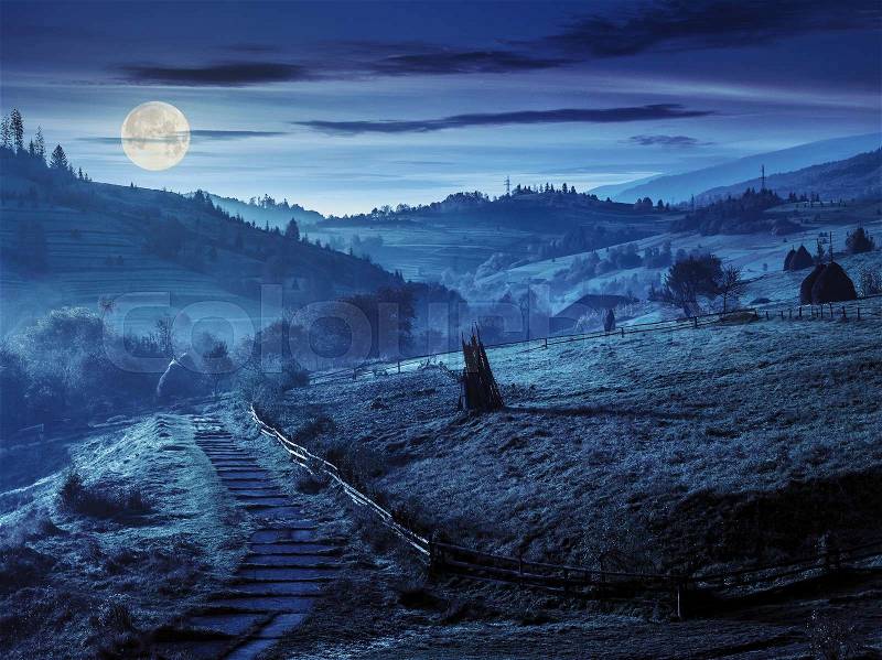 Stone steps down the hill in to village in foggy mountains at night in full moon light, stock photo