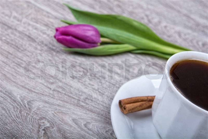 A cup of coffee with cinnamon and purple tulips on a wooden background, stock photo