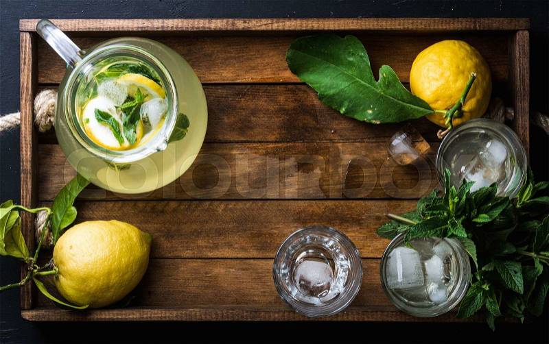 Homemade lemonade with mint and ice, served with fresh lemons over wooden background, top view, copy space. Food frame , stock photo
