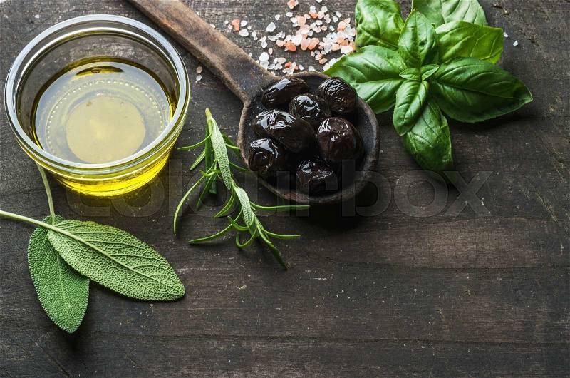 Greek black olives, fresh green sage, rosemary, basil herbs, salt and oil on dark rustic wooden background. Top view, copy space, stock photo