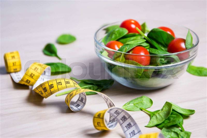 Diet and weight loss concept - healthy salad with spinach and tomatoes and measure tape, stock photo