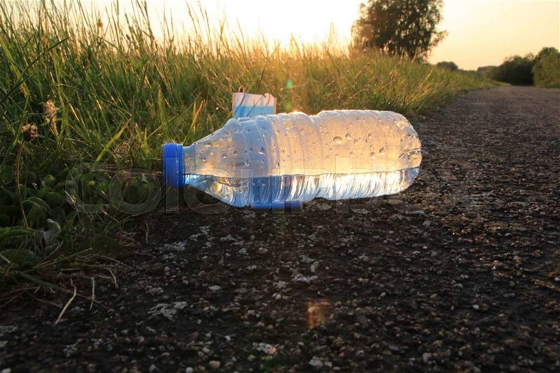Lost, a plastic bottle with a screw cap and half empty with mineral water by a runner in the park at sunset, stock photo