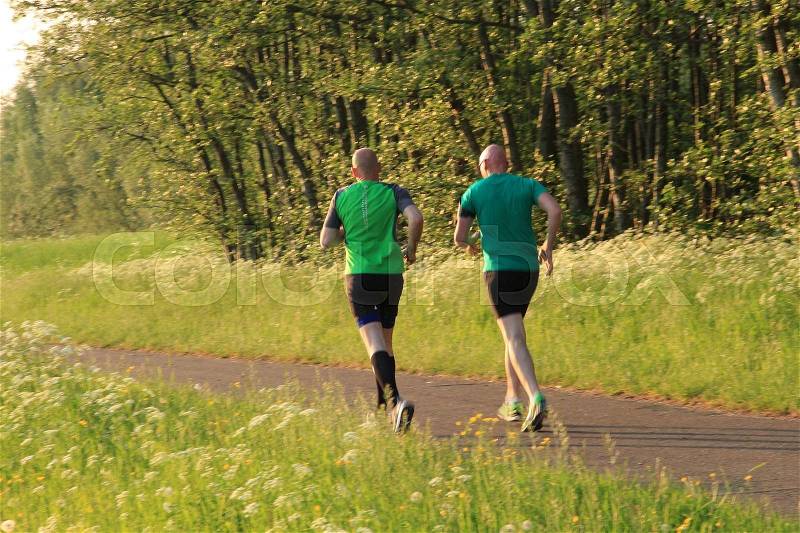 The two runners are in training for the marathon in the park at sunset in the summer, stock photo