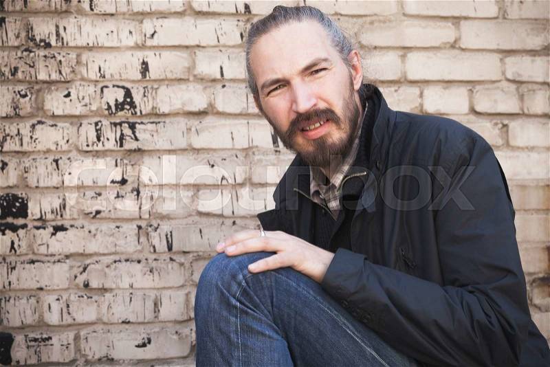 Outdoor portrait of young bearded Asian man in black over gray urban grungy brick wall background, stock photo