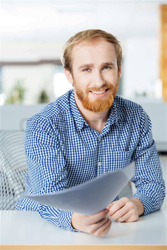 Cheerful businessman sitting in office and giving papers to you, stock photo