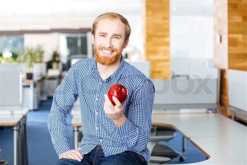 Happy handsome young businessman siting in office and holding red apple , stock photo
