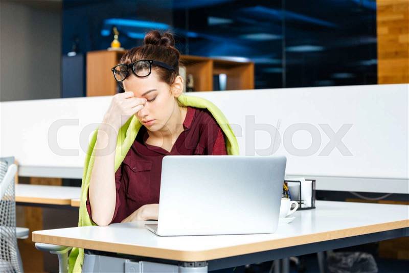 Tired beautiful young business woman in glasses working with laptopon workplace, stock photo