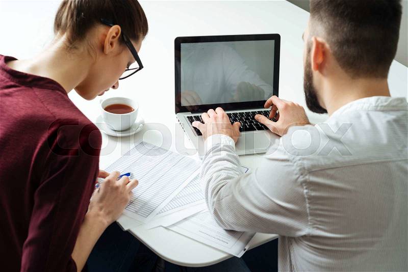 Back view of two focused serious businesspeople using laptop together in meetin room, stock photo