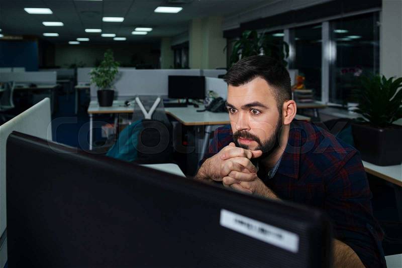 Handsome bearded young businessman sitting on workplace and working late , stock photo