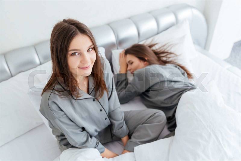 Closeup of two sleepy cute young sisters twins on bed in bedroom, stock photo