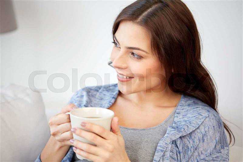 People, drinks and leisure concept - happy young woman with cup of tea or coffee at home, stock photo