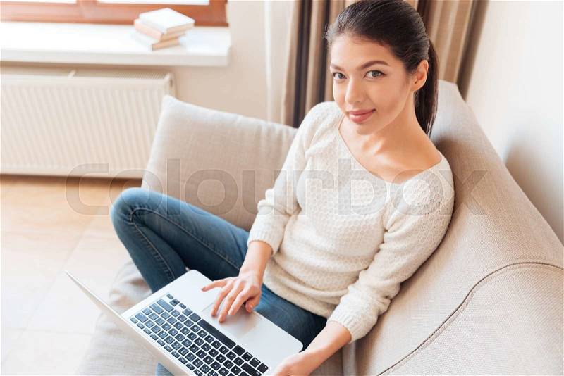 Beautiful woman sitting on the sofa with laptop and looking at camera , stock photo