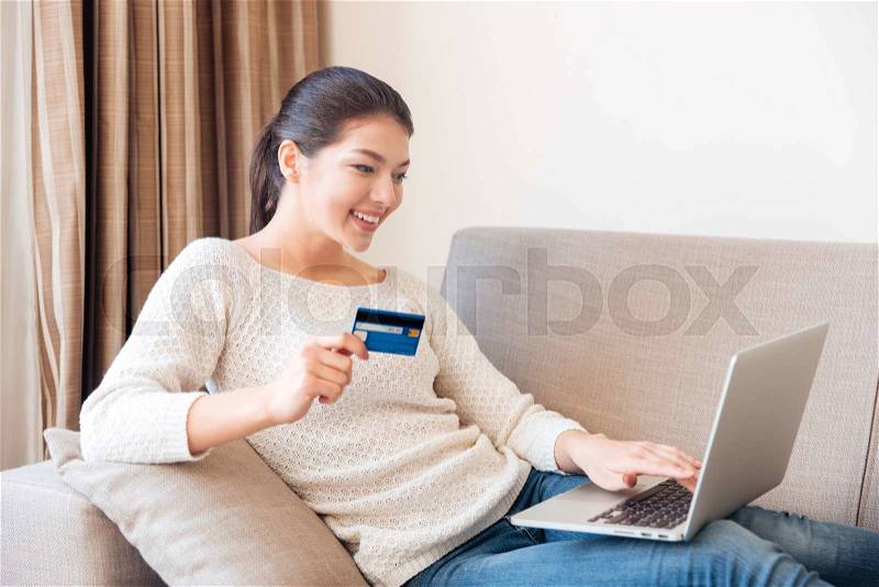 Happy woman buying online on laptop computer with credit card at home, stock photo