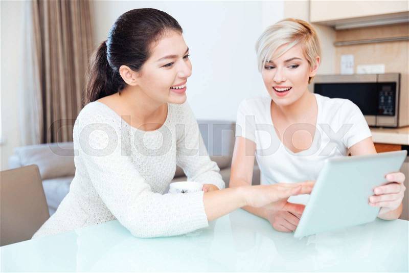 Happy two girlfriends using tablet computer on the kitchen, stock photo