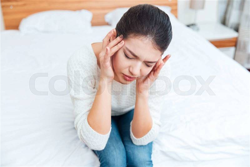 Woman sitting on the bed and having head pain at home, stock photo