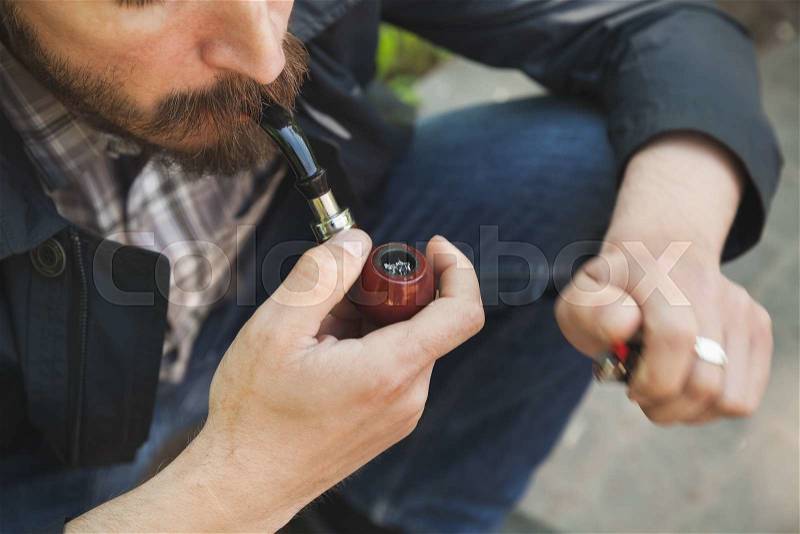 Bearded man smoking pipe, outdoor photo with selective focus, stock photo