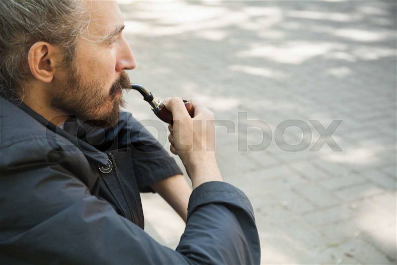Bearded man smoking pipe, outdoor portrait with selective focus, stock photo