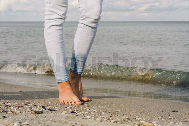 Female feet in jeans barefoot walk on the sea water on the beach, stock photo