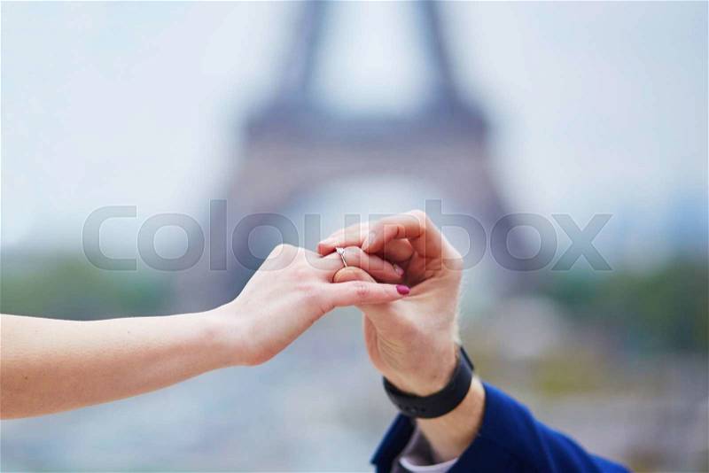 Romantic engagement in Paris, man proposing to his girlfriend near the Eiffel tower. Surprise proposal or elopement concept, stock photo