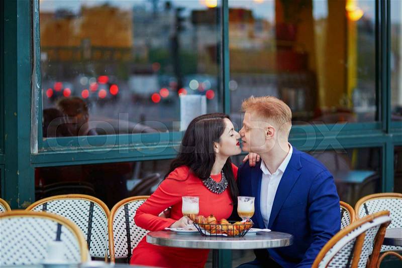 Happy couple drinking coffee and kissing in an outdoor cafe in Paris. Tourists enjoying their vacation in France. Romantic date or traveling couple concept, stock photo