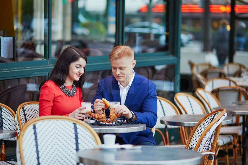 Happy couple drinking coffee in an outdoor cafe in Paris. Tourists enjoying their vacation in France. Romantic date or traveling couple concept, stock photo