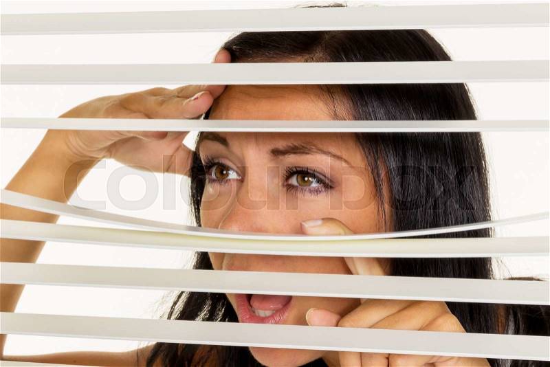 A young woman watching something through the blinds of her window, stock photo