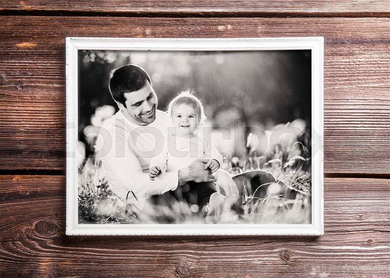 Fathers day composition. Photo of father and son in white picture frame. Studio shot on wooden background, stock photo