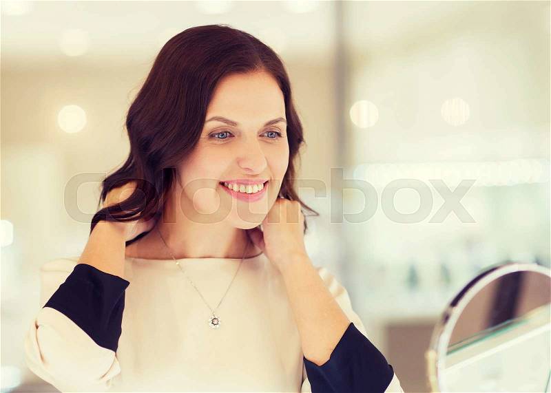 Sale, consumerism, shopping and people concept - happy woman choosing and trying on pendant at jewelry store, stock photo